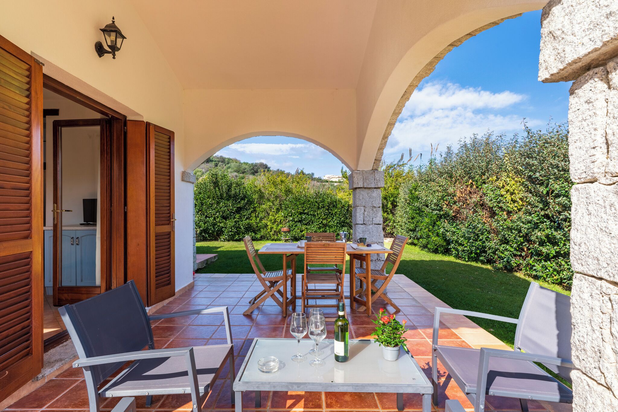 An outdoor patio with a table, chairs, and a bottle of wine.