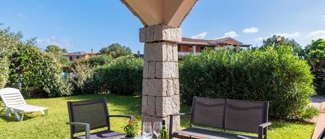 Un patio al aire libre con un pilar de piedra, dos sillas, una mesa y una botella de vino.