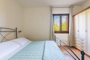 A bedroom with a bed, a window with a view of greenery, a wardrobe, and a door. - Residence Vecchio Stazzo (San Teodoro)