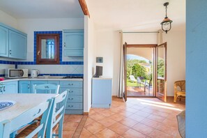 Cozinha com armários azuis, micro-ondas e mesa de jantar com cadeiras.