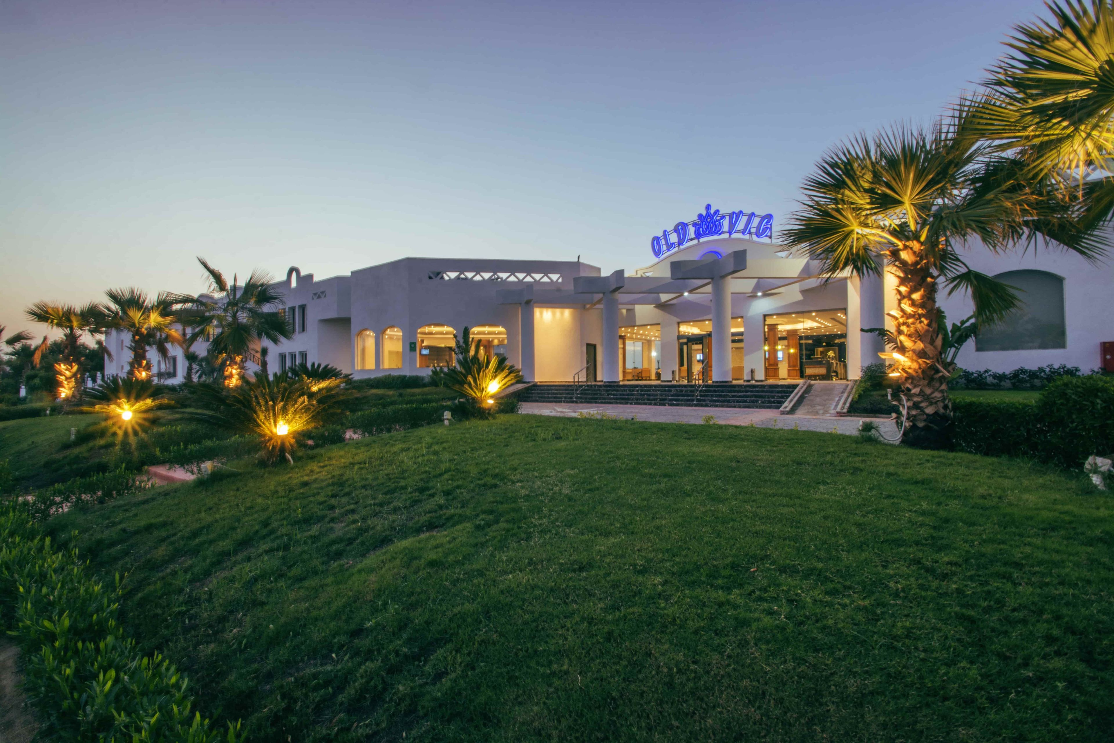 A hotel with a modern architectural design, featuring a prominent entrance with a covered walkway and palm trees in the foreground.