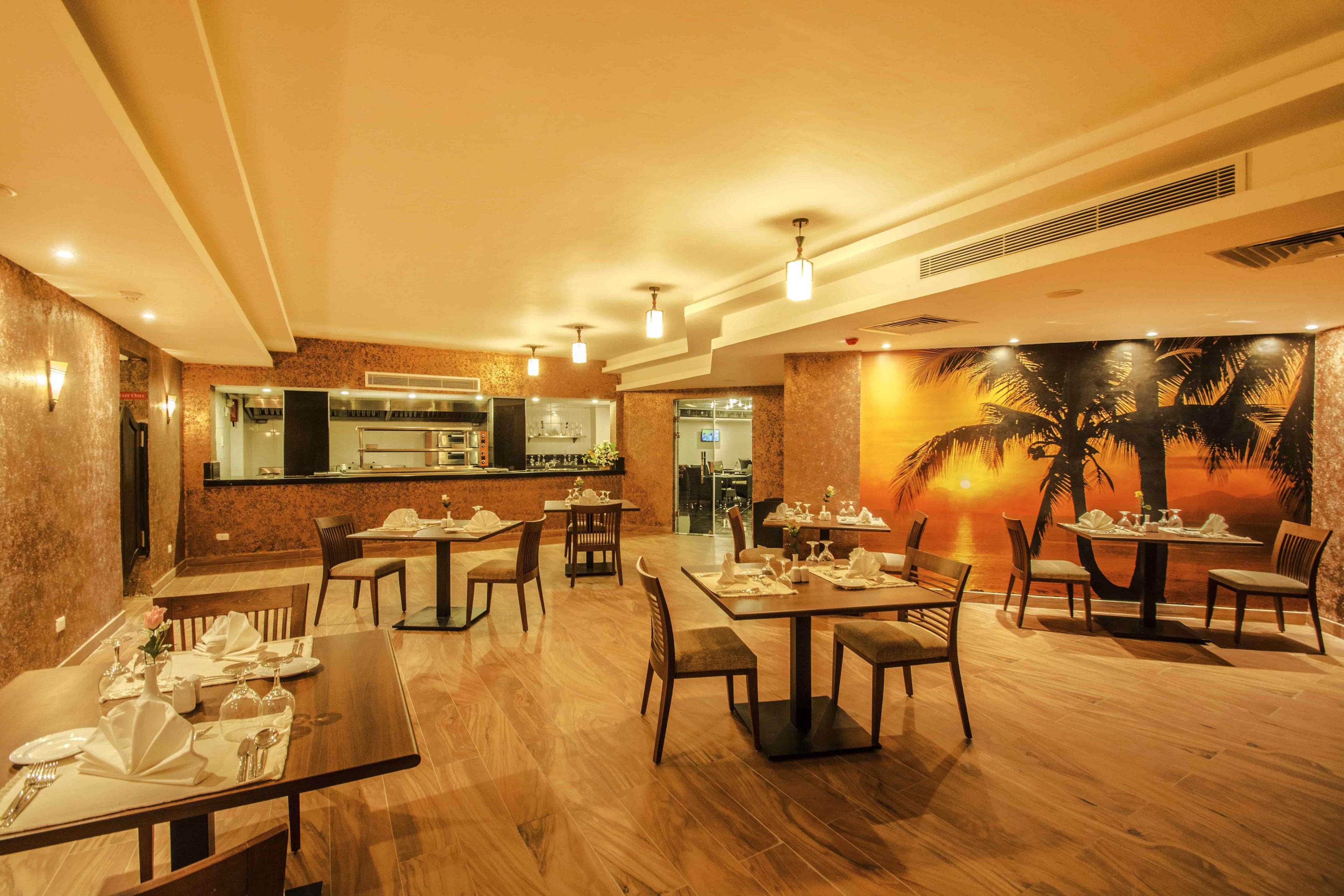 A restaurant with wooden tables and chairs, a bar area, and a mural of a sunset with palm trees.