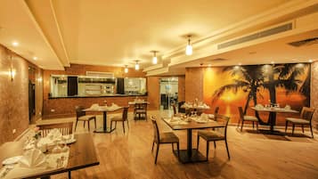 A restaurant with wooden tables and chairs, a bar area, and a mural of a sunset with palm trees.
