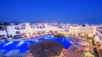 A hotel with a large swimming pool, multiple lounge areas, and a well-lit outdoor space.