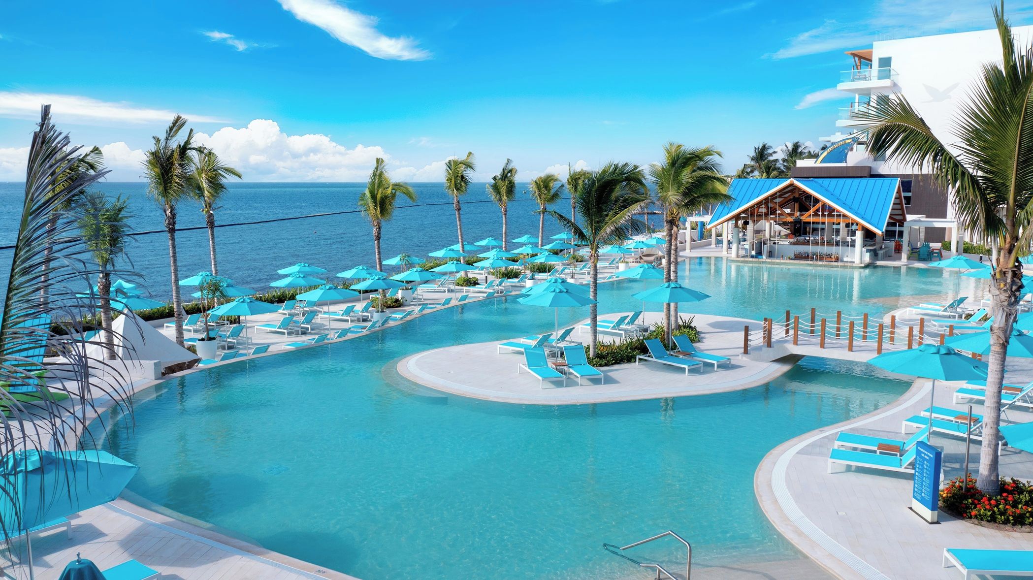 A resort pool with clear blue water, surrounded by palm trees and lounge chairs.