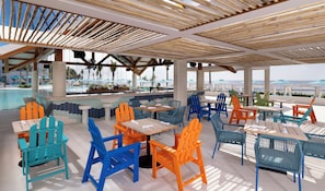 Un espacio al aire libre con sillas y mesas coloridas, con vista a una piscina y una playa.