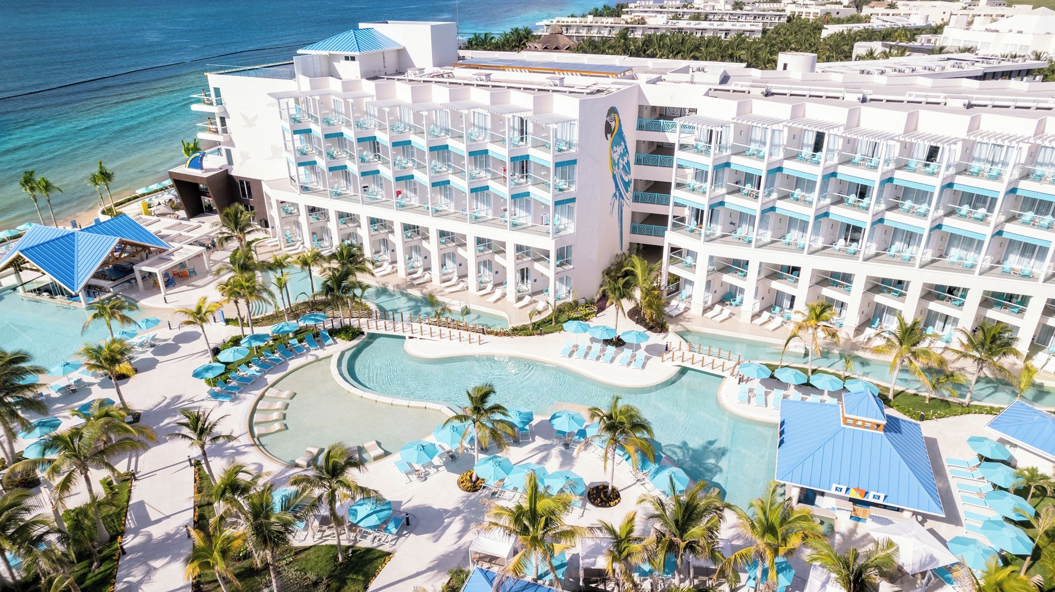 Een resort met verschillende zwembaden, ligbedden en een groot gebouw met balkons.
