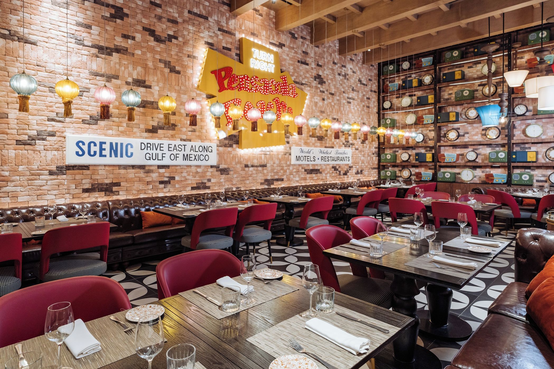 A restaurant with brick walls, vintage clocks, and red chairs. Tables are set with wine glasses and plates.