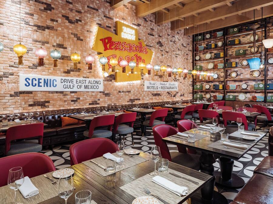 A restaurant with brick walls, vintage clocks, and red chairs. Tables are set with wine glasses and plates.