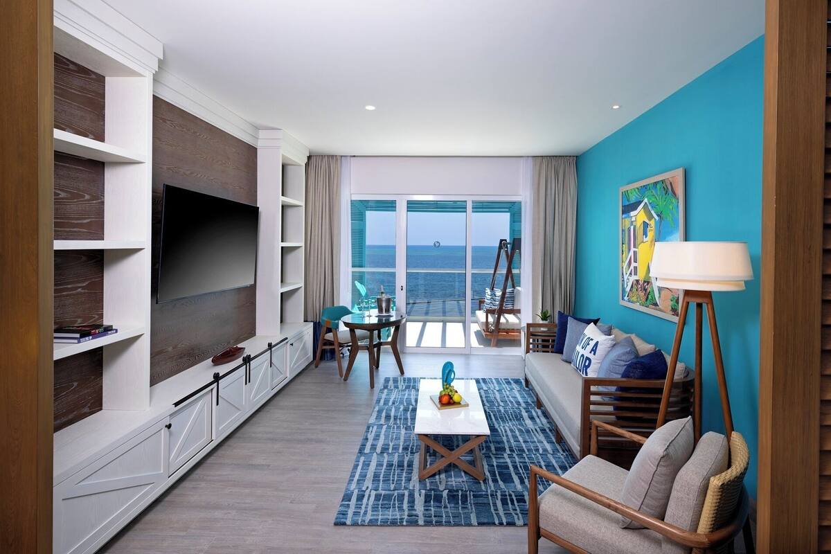 Una sala de estar moderna con un televisor grande, un comedor y vistas al océano.