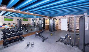 A gym with various exercise equipment, a television mounted on the wall, and a brick wall. - Margaritaville Island Reserve Riviera Maya (Puerto Morelos)
