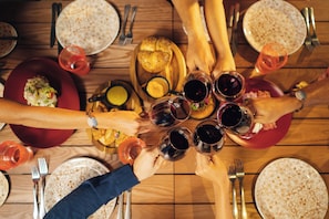 Un groupe de personnes trinquant avec des verres de vin autour d’une table en bois, où sont disposées des assiettes de nourriture et des couverts.