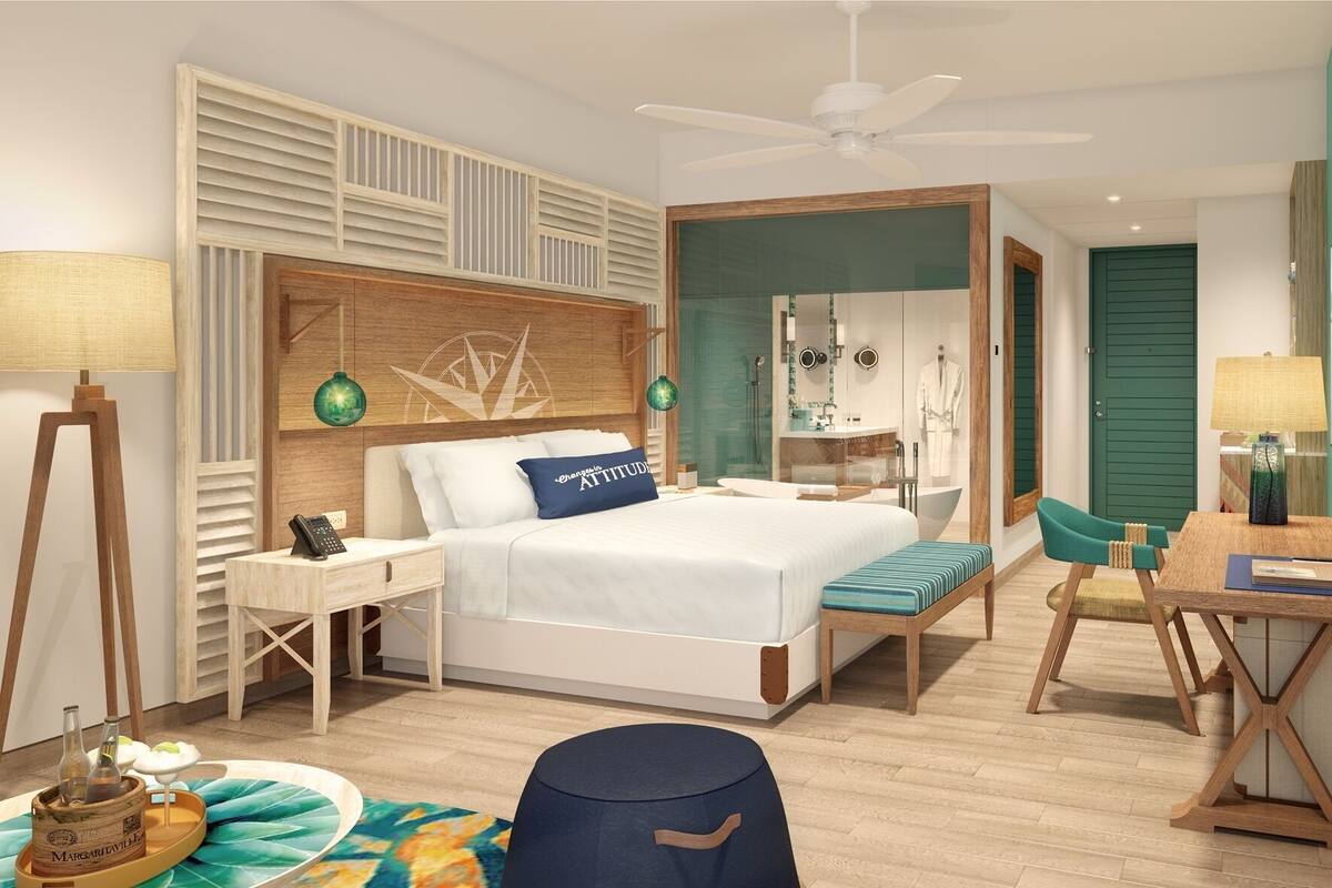 Un dormitorio moderno con cama, mesita de noche, escritorio, silla y un baño visible a través de una puerta abierta.