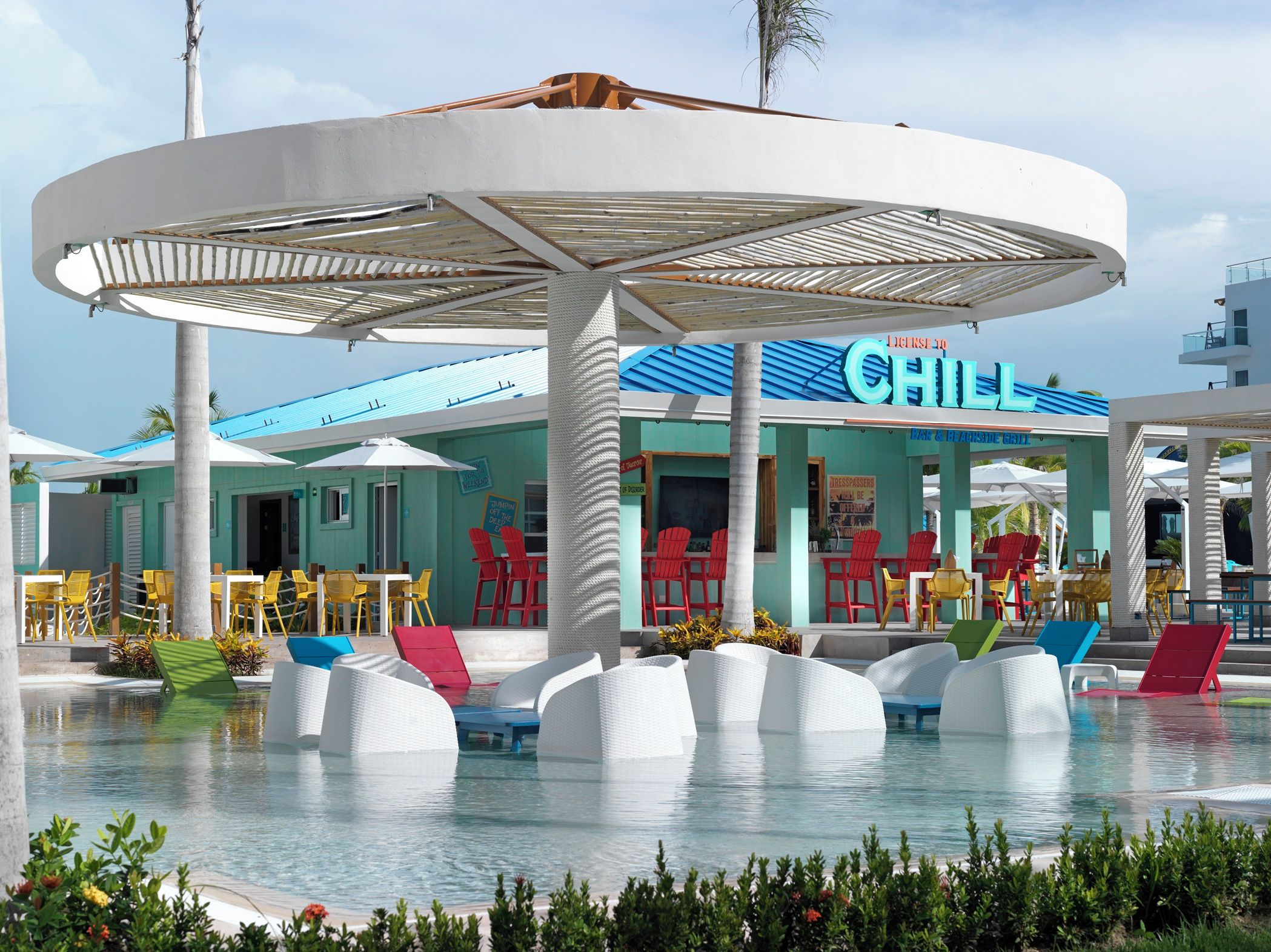 A pool area with white lounge chairs, a covered seating area, and a restaurant named "Chill".