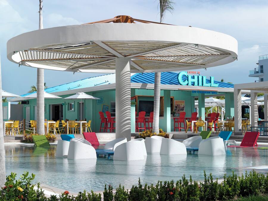 A pool area with white lounge chairs, a covered seating area, and a restaurant named "Chill".