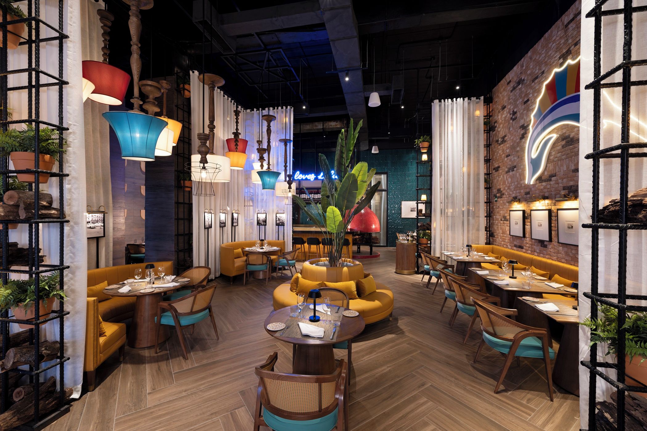 A restaurant interior with wooden flooring, yellow seating, and various hanging lights.