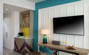 A hotel room with a kitchenette, a flat-screen TV mounted on the wall, a desk with a lamp, and a chair. - Margaritaville Island Reserve Riviera Maya (Puerto Morelos)