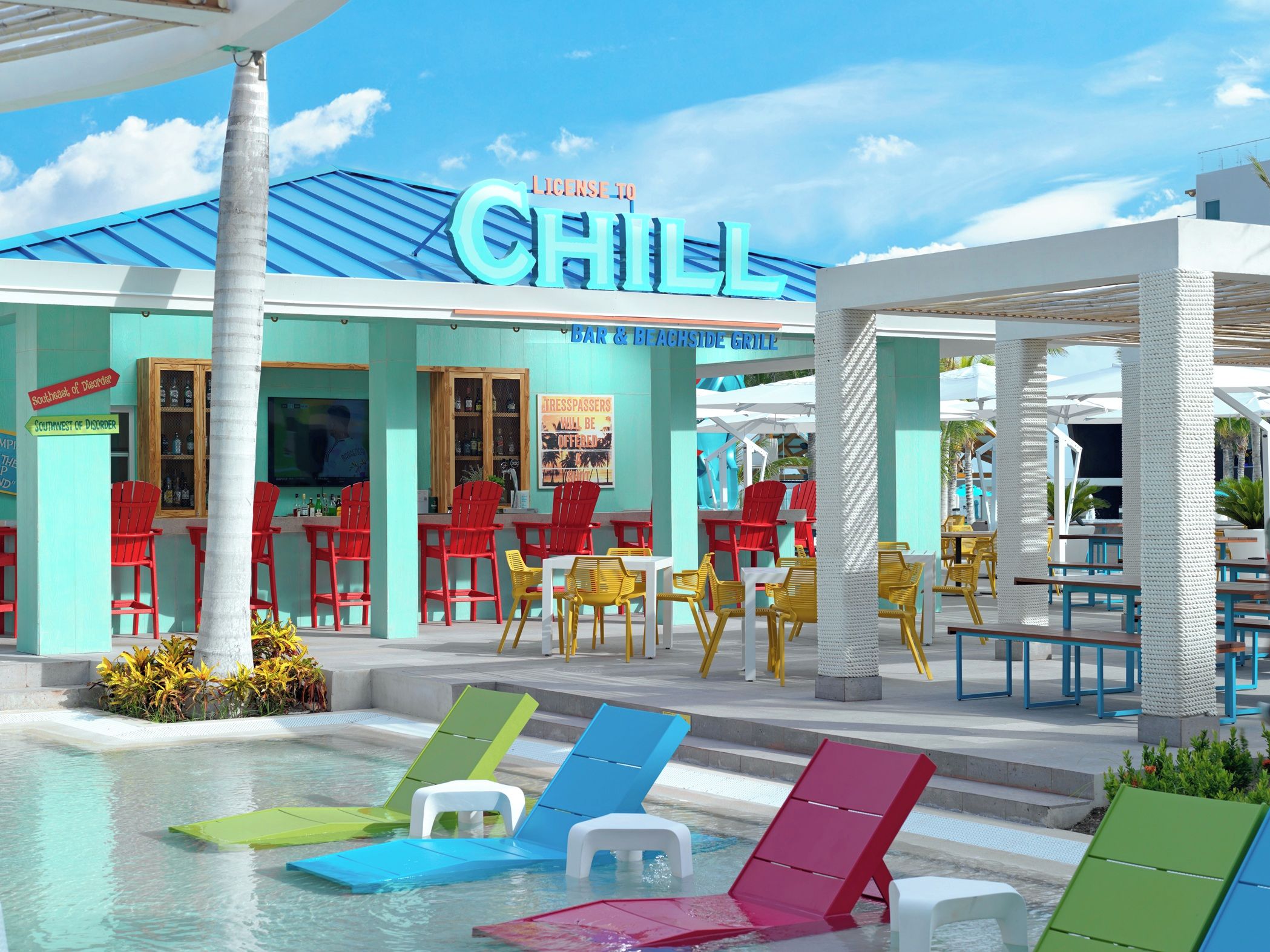 A poolside area with colorful lounge chairs, a bar and beachside grill, and a building with a 'CHILL' sign.