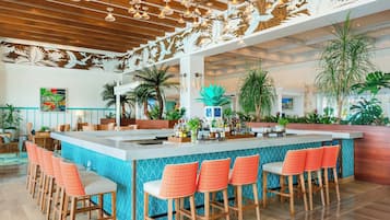 A bar area with a long counter, multiple bar stools, and a variety of plants.