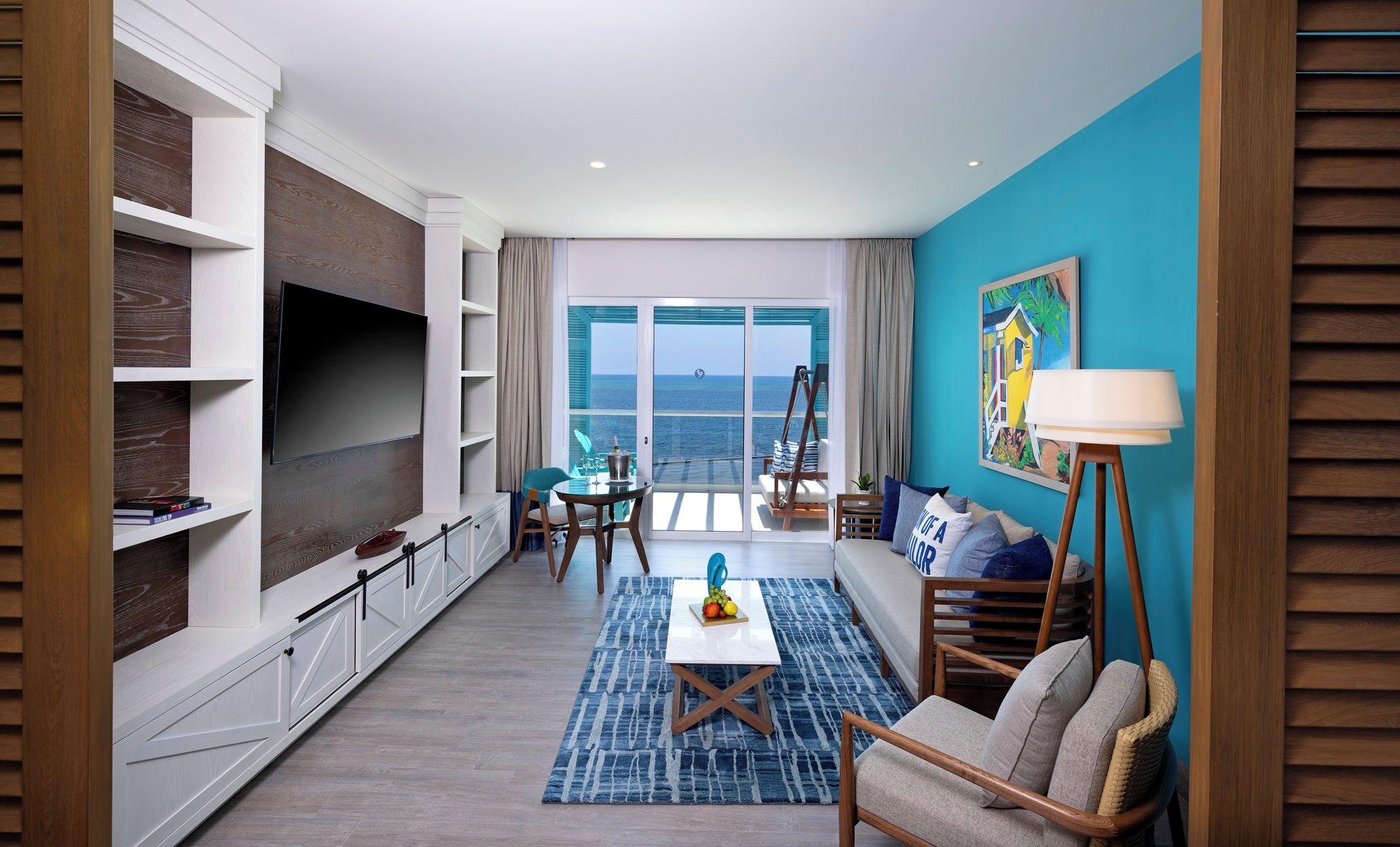 A modern living room with a large TV, a dining area, and a view of the ocean.