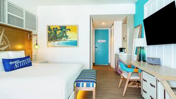 A hotel room with a bed, a desk, a chair, a TV, and a painting of a beach scene.
