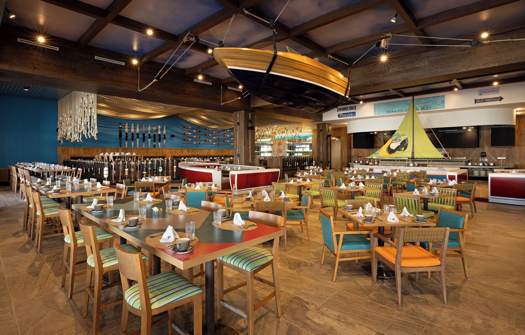 Une grande salle à manger avec de nombreuses tables et chaises, un coin bar et un présentoir de cannes à pêche accroché au mur.