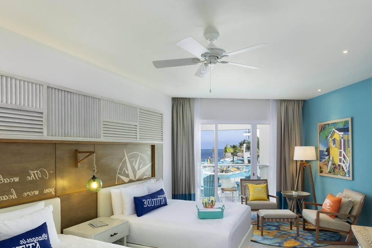Habitación de hotel con cama, escritorio, silla, televisor y vista a la playa y la piscina.