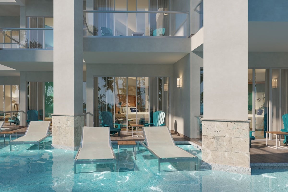 Un área de piscina con varios niveles, sillas de descanso y una habitación con cama, cerrada con vidrio.