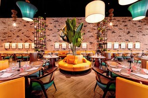A restaurant with round tables, orange seating, and a brick wall. - Margaritaville Island Reserve Riviera Maya (Puerto Morelos)