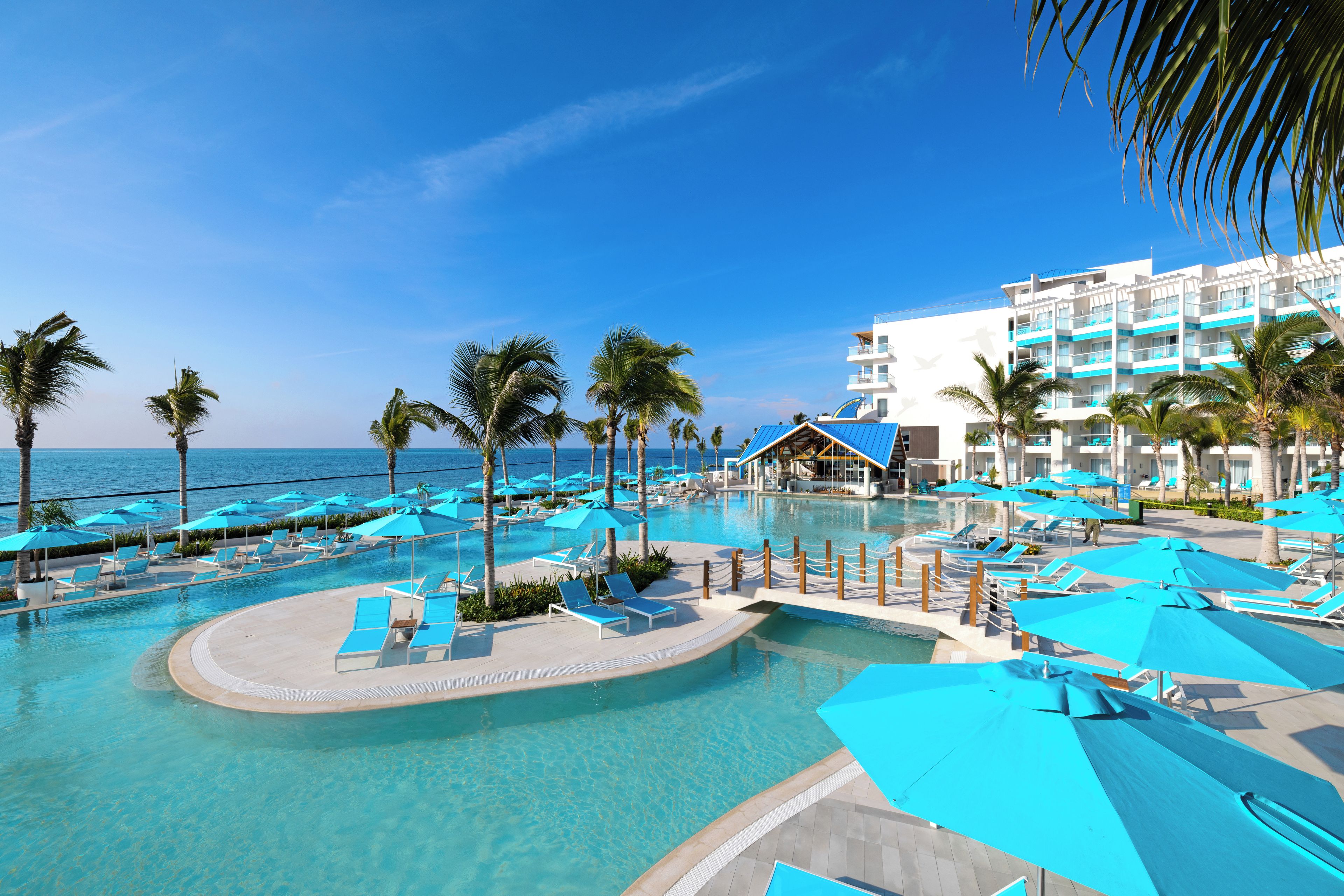 A resort pool area with clear blue water, lounge chairs, and umbrellas.