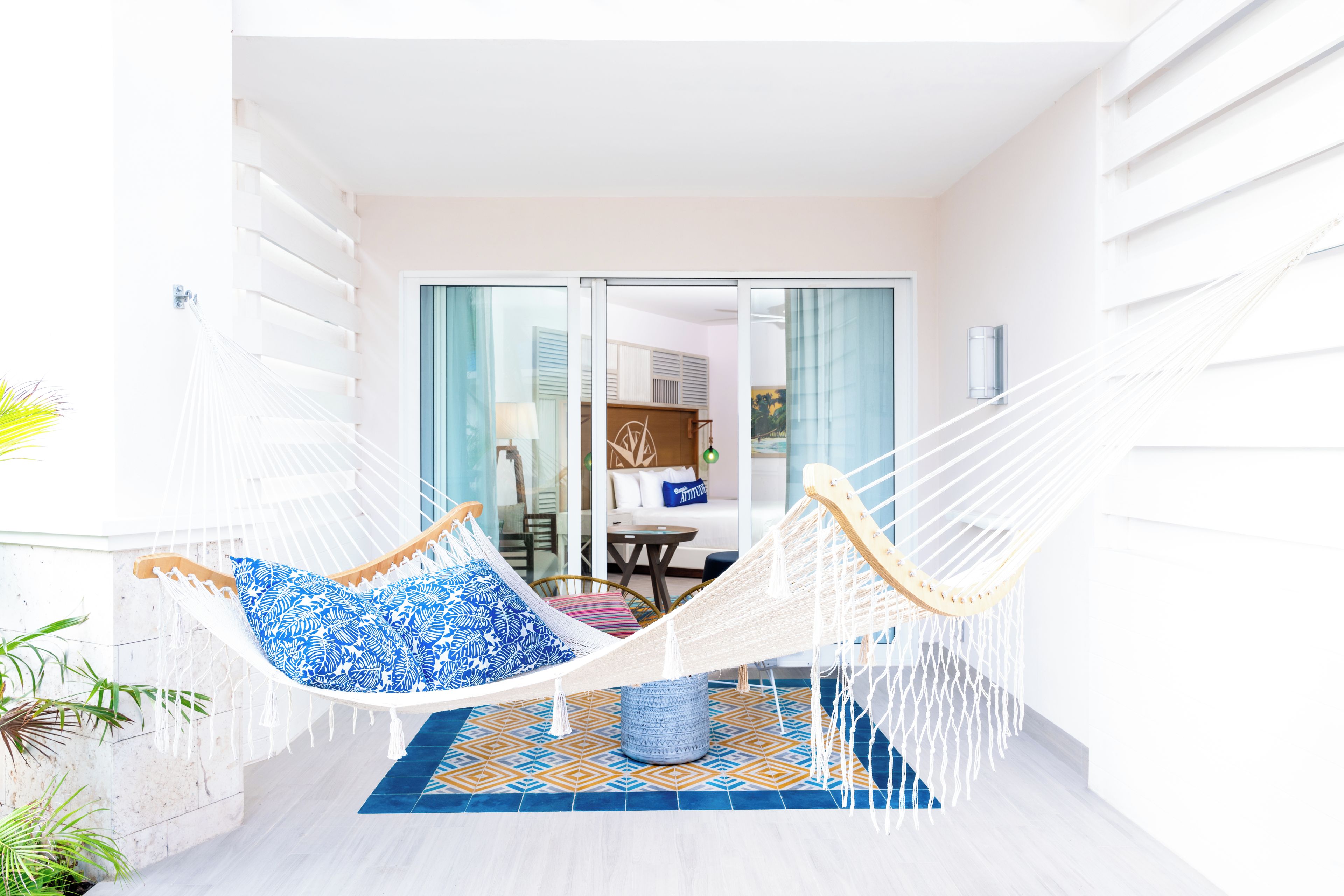 Een hangstoel met blauw gestreepte kussens in een lichte kamer met een betegelde vloer en uitzicht op een eetgedeelte door glazen deuren.