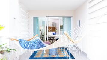 Een hangstoel met blauw gestreepte kussens in een lichte kamer met een betegelde vloer en uitzicht op een eetgedeelte door glazen deuren.