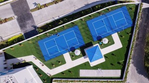 An aerial view of a sports facility with two tennis courts, surrounded by green lawns and pathways. - Margaritaville Island Reserve Riviera Maya (Puerto Morelos)