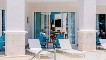 A poolside area with white lounge chairs, a blue chair, and a table with a lamp.