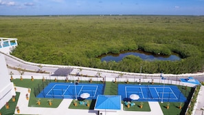 Vue aérienne d’un hôtel doté de plusieurs courts de tennis, d’une grande étendue d’eau et d’un environnement verdoyant.