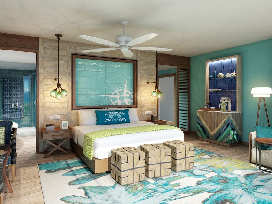 A modern hotel room with a large bed, a ceiling fan, a wall-mounted compass, and a view of the sea through a window.