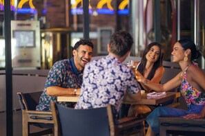 A group of people seated at an outdoor table in a restaurant with a modern interior and large windows. - Margaritaville Island Reserve Riviera Maya (Puerto Morelos)