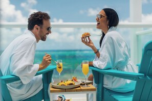 A couple dining at a table with a view of the ocean, a plate of food, and two drinks. - Margaritaville Island Reserve Riviera Maya (Puerto Morelos)