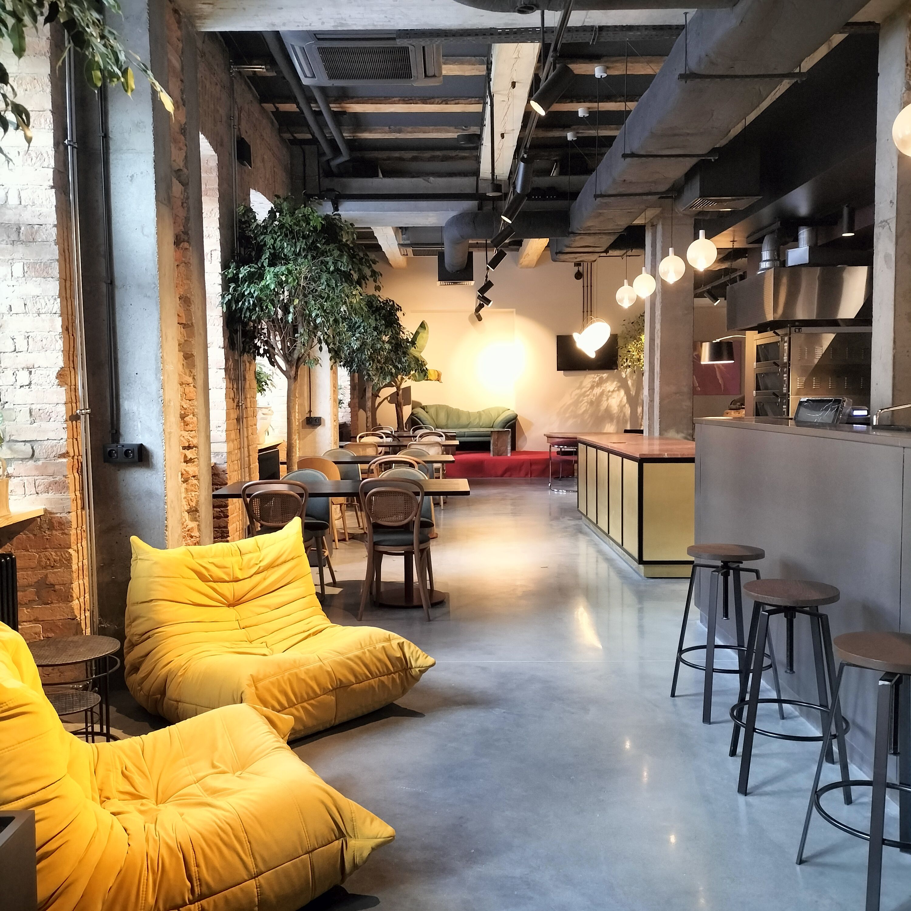 A modern interior with exposed brick walls, a green sofa, wooden chairs, and a bar area with stools.
