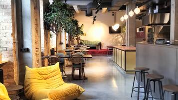 A modern interior with exposed brick walls, a green sofa, wooden chairs, and a bar area with stools.