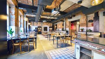 Um restaurante espaçoso com paredes de tijolos aparentes, vigas de teto industriais e uma mistura de móveis de madeira e metal.