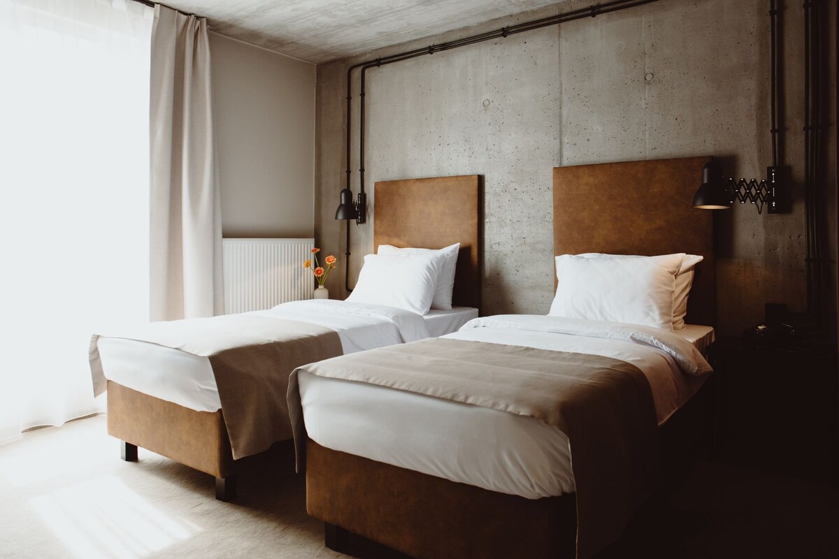 A hotel room with two beds, a concrete wall, and a radiator.