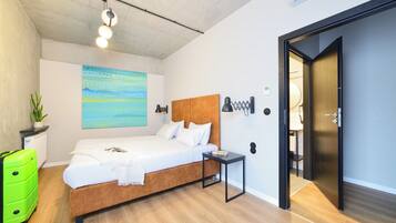Um quarto moderno com uma cama de madeira, uma mesinha de cabeceira, uma mala verde vibrante e um quadro na parede.