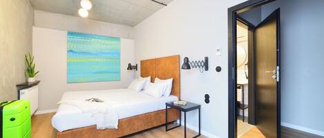 Um quarto moderno com uma cama de madeira, uma mesinha de cabeceira, uma mala verde vibrante e um quadro na parede.