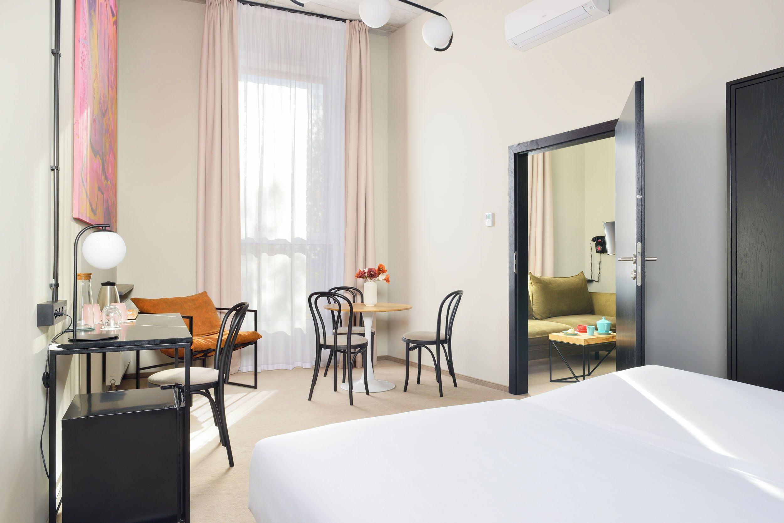 Habitación de hotel con cama, escritorio con lámpara, silla, pequeña mesa con un florero y sofá.