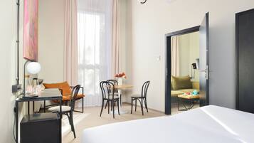 A hotel room with a bed, a desk with a lamp, a chair, a small table with a vase of flowers, and a sofa.
