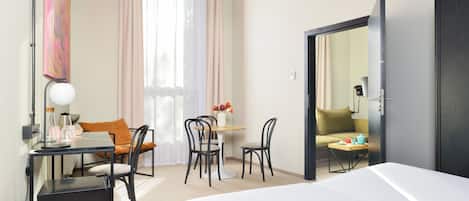 A hotel room with a bed, a desk with a lamp, a chair, a small table with a vase of flowers, and a sofa.