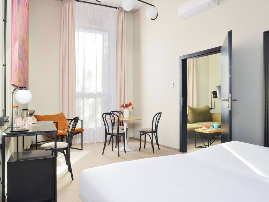 Habitación de hotel con cama, escritorio con lámpara, silla, pequeña mesa con un florero y sofá.