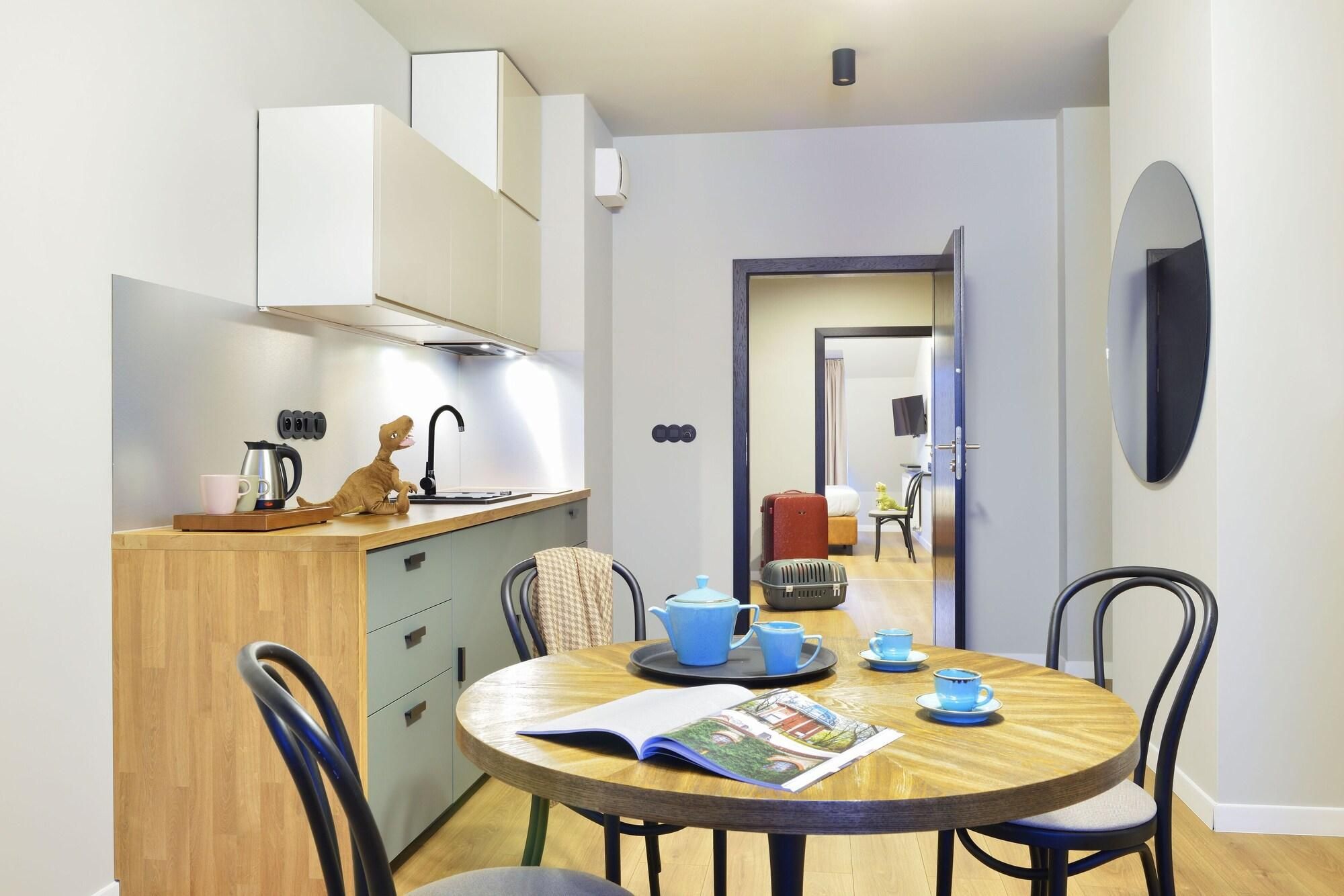 A compact kitchen with modern appliances, a dining area with a round table and chairs, and a visible doorway leading to a living space.