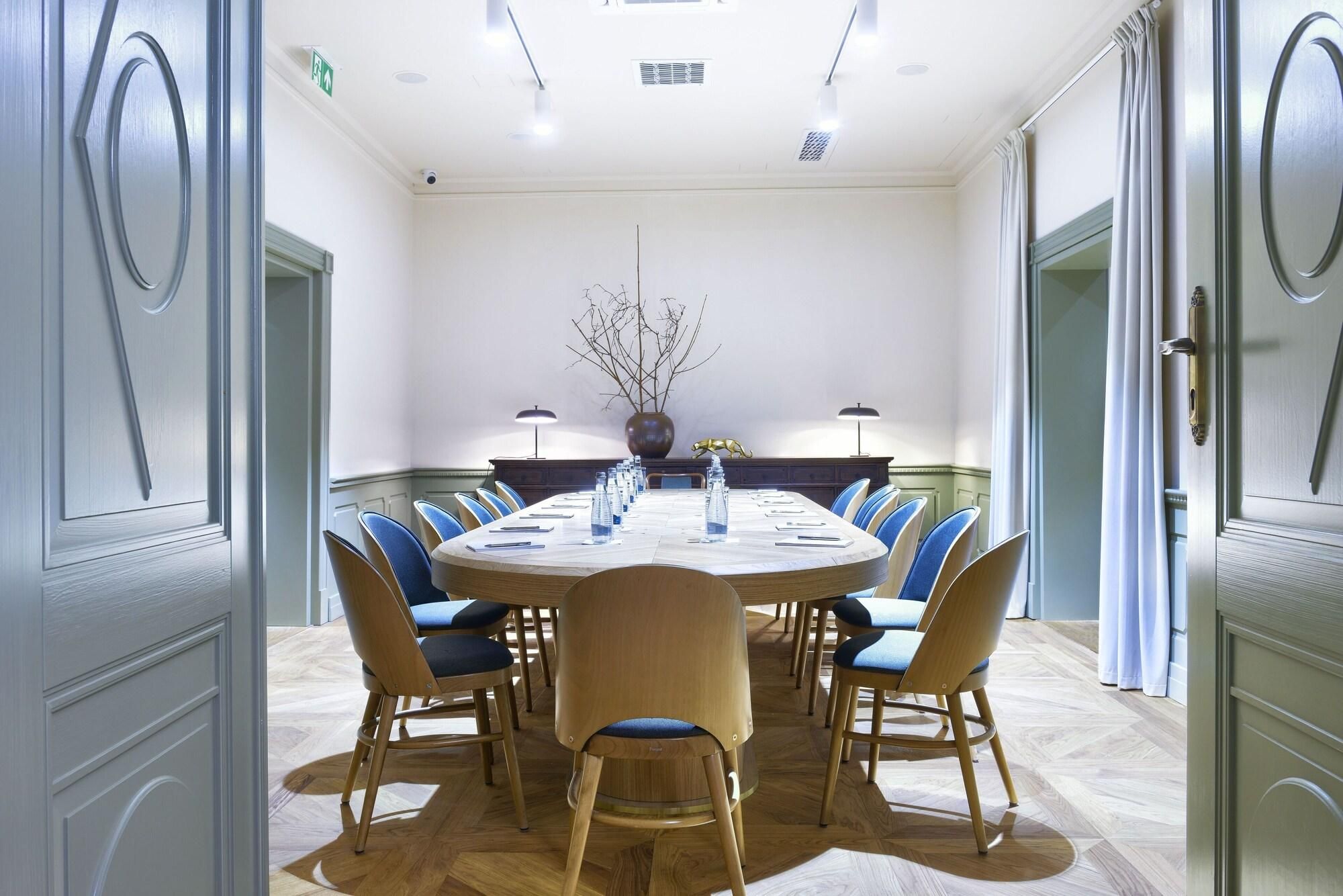 A conference room with a round table, blue upholstered chairs, and a wooden cabinet with a lamp.